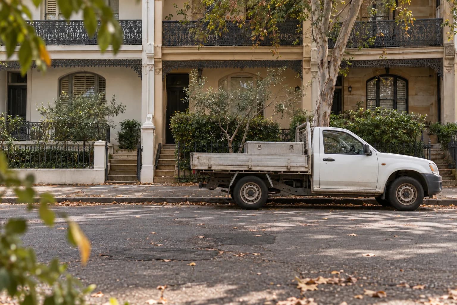 A white work ute is parked beneath gum trees outside Sydney terrace houses.